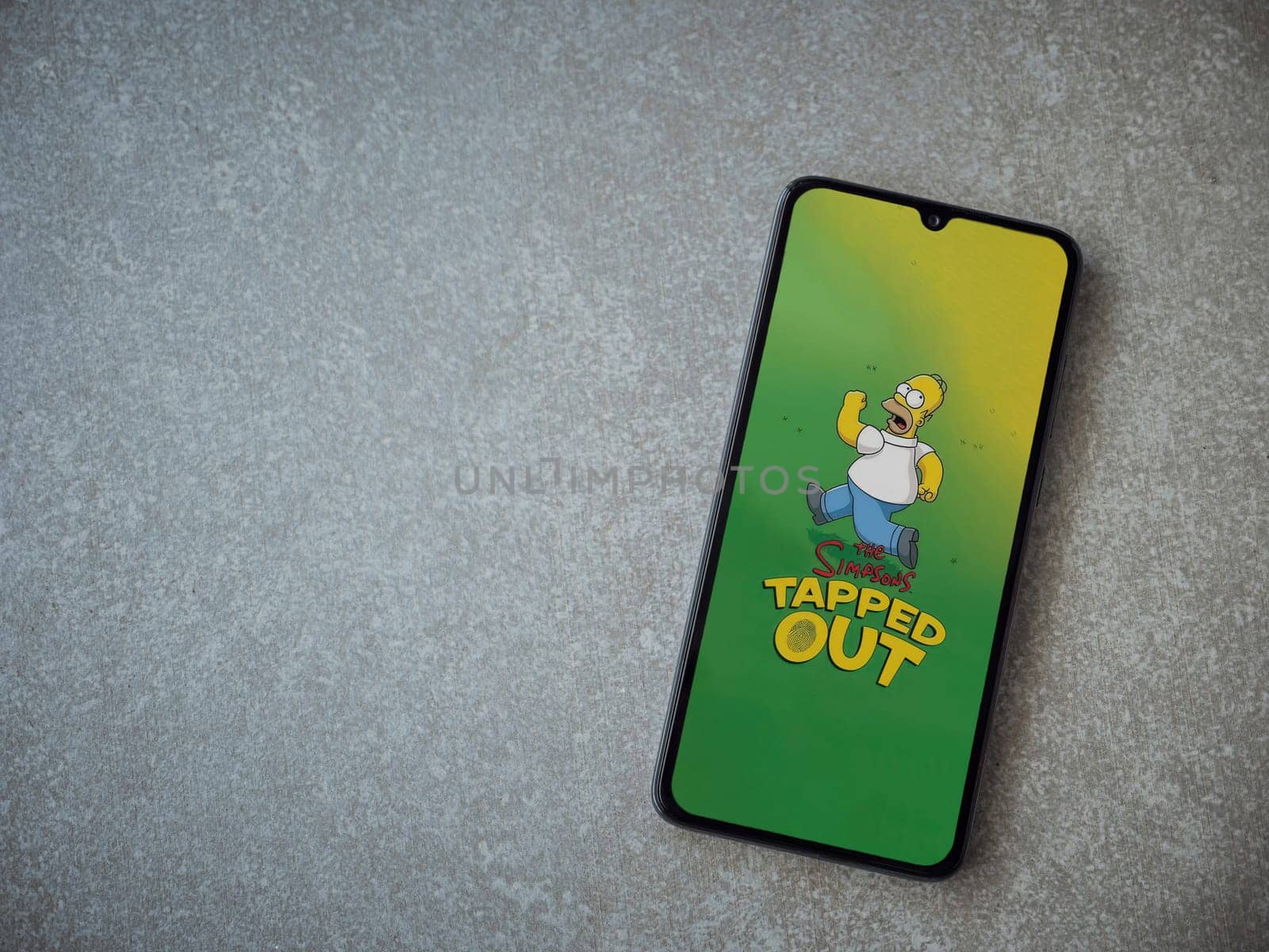 Lod, Israel - July 16,2023: The Simpsons Tapped Out app launch screen on smartphone on ceramic stone background. Top view flat lay with copy space.