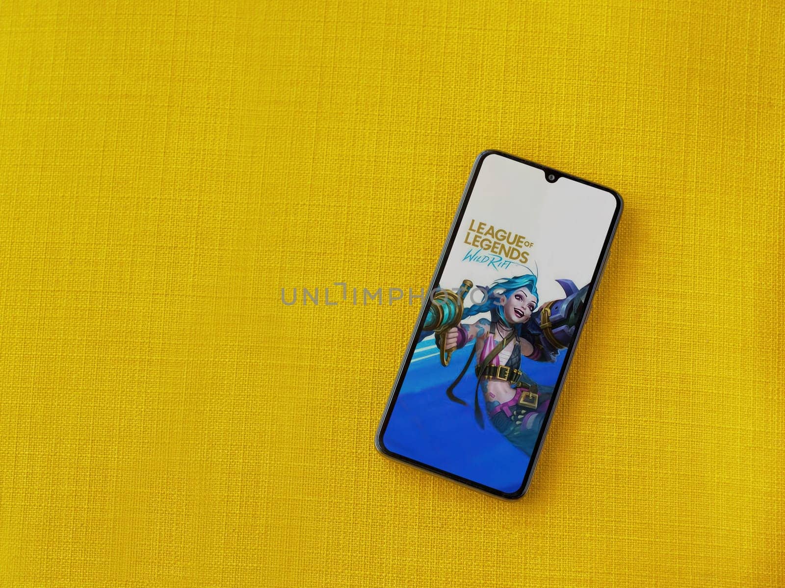 Lod, Israel - July 16,2023: League of Legends - Wild Rift app launch screen on smartphone on yellow fabric background. Top view flat lay with copy space.
