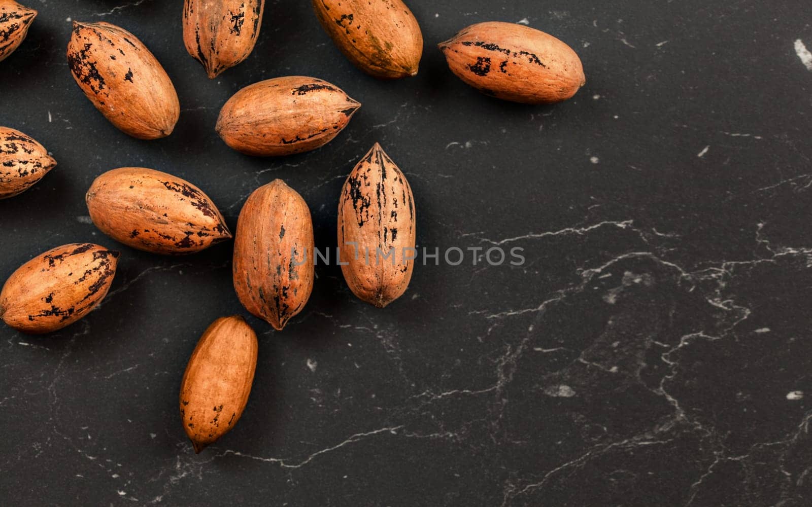 Whole pecan nuts on black marble board, flat lay photo with space for text down right