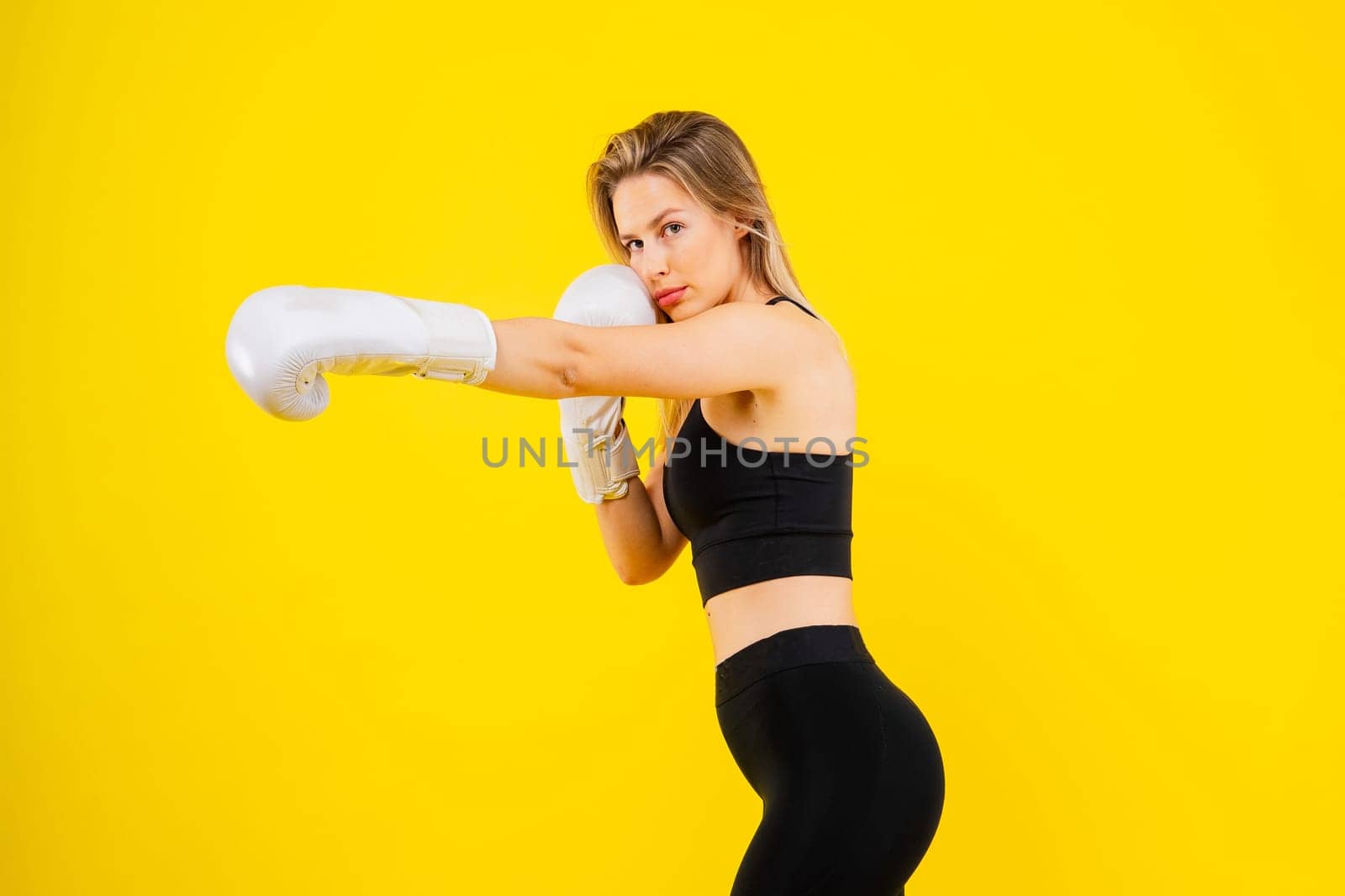 Woman boxer in gloves training on a yellow and dark studio background