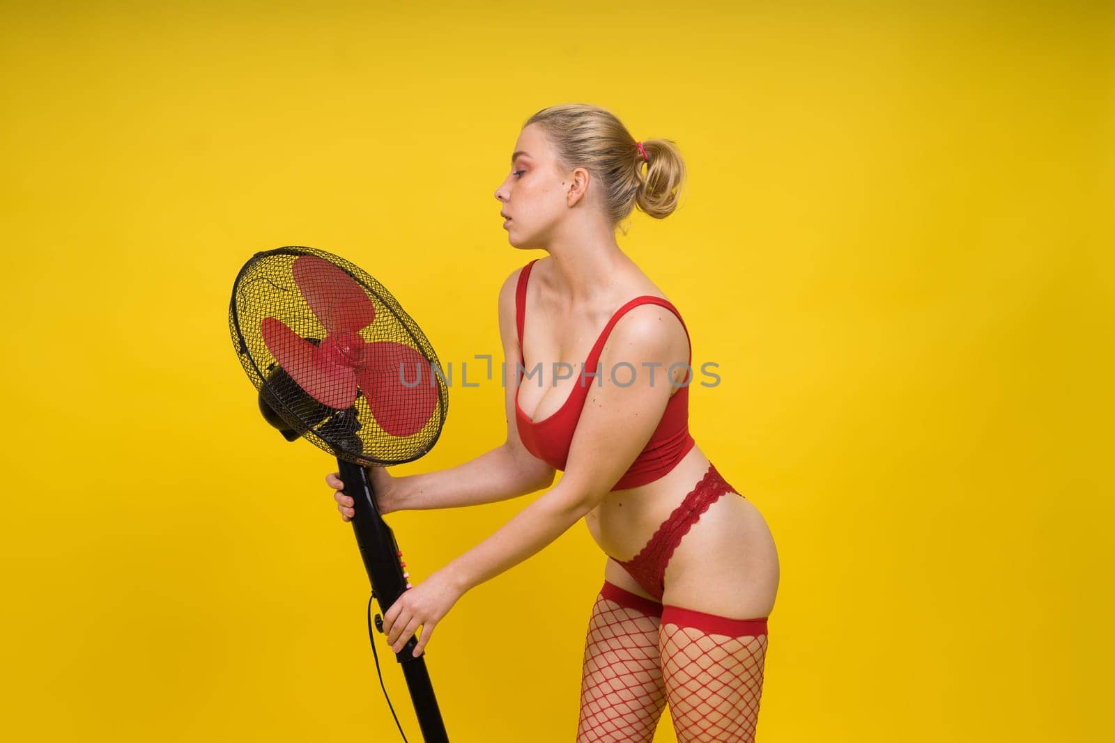 Professional fashion model blonde woman posing sitting in a red lingerie with big fan