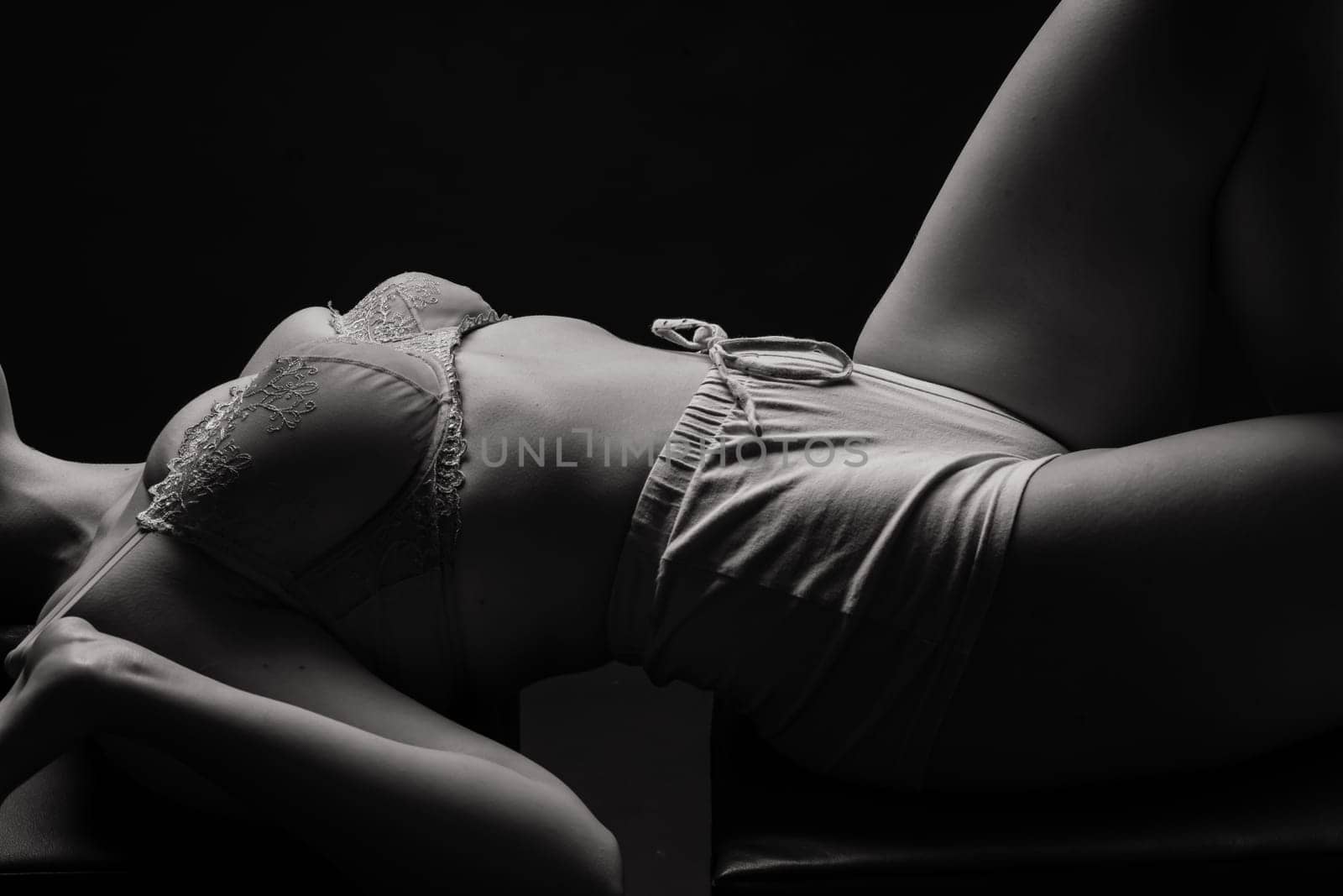 Elegant blonde woman in a studio lying over dark background wearing lingerie and naked
