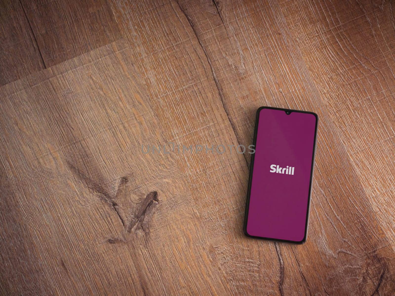 Lod, Israel - July 16,2023: Skrill app launch screen on smartphone on wooden background. Top view flat lay with copy space.