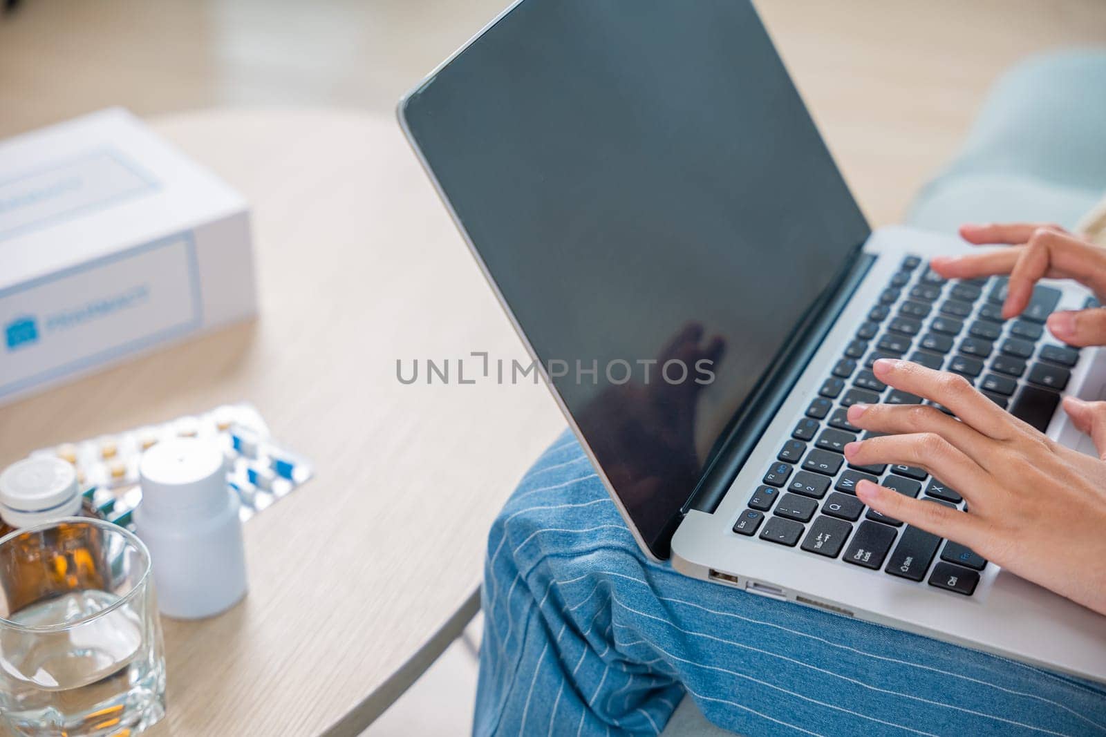 Business female sick she taking pills for flu while work with laptop keyboard, Asian sick woman covered blanket suffering from covid-19 virus but still working at home with laptop computer
