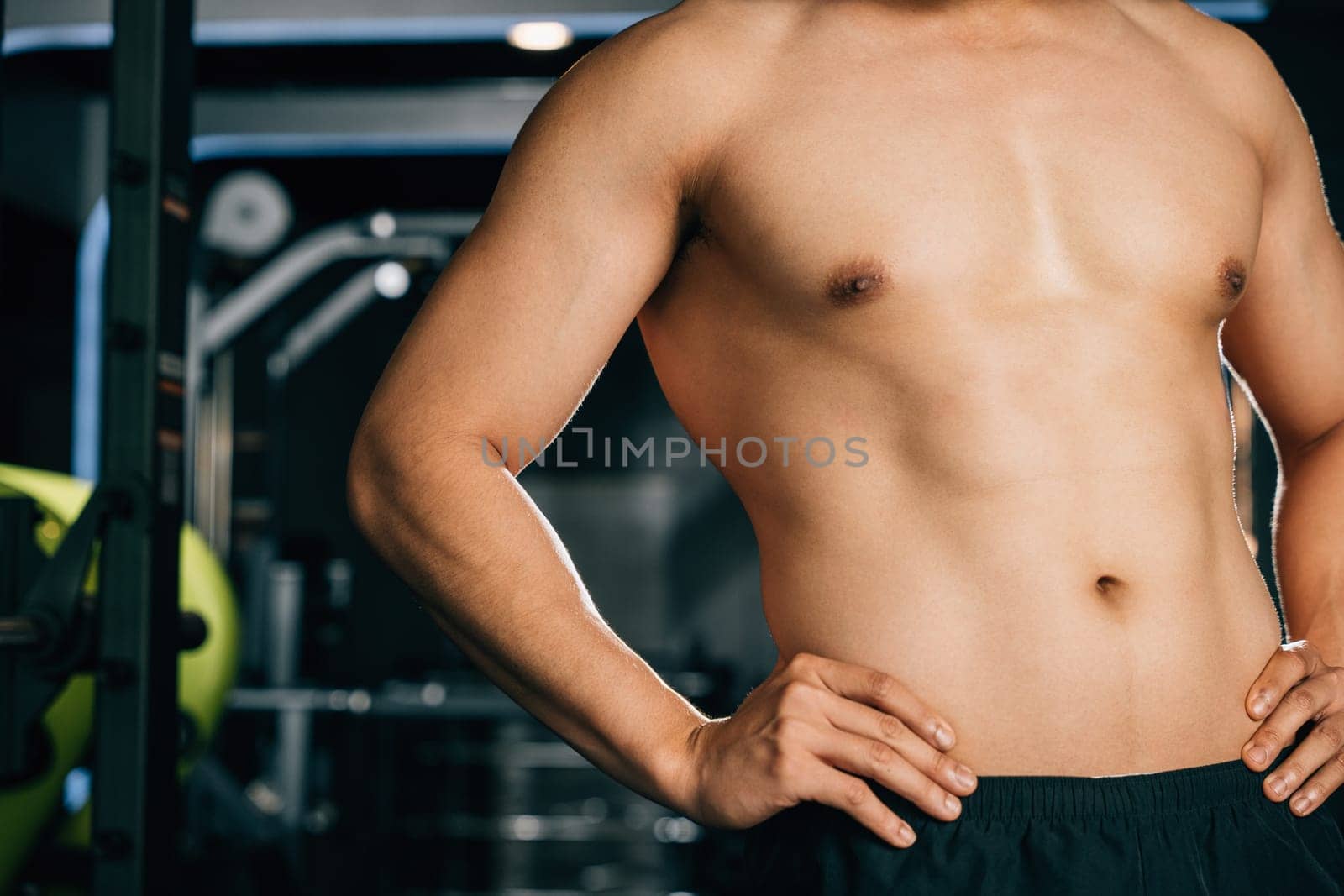 A handsome macho man, with a muscular chest and arms, stands in a gym interior, looking at his trainer with a cheerful attitude during his workout. Healthy fitness Lifestyle with copy space