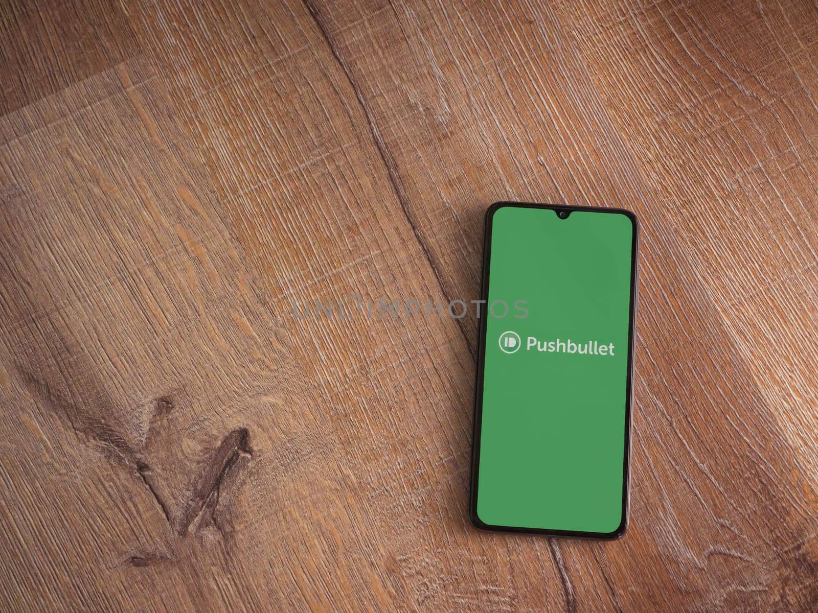 Lod, Israel - July 16,2023: Pushbullet app launch screen on smartphone on wooden background. Top view flat lay with copy space.