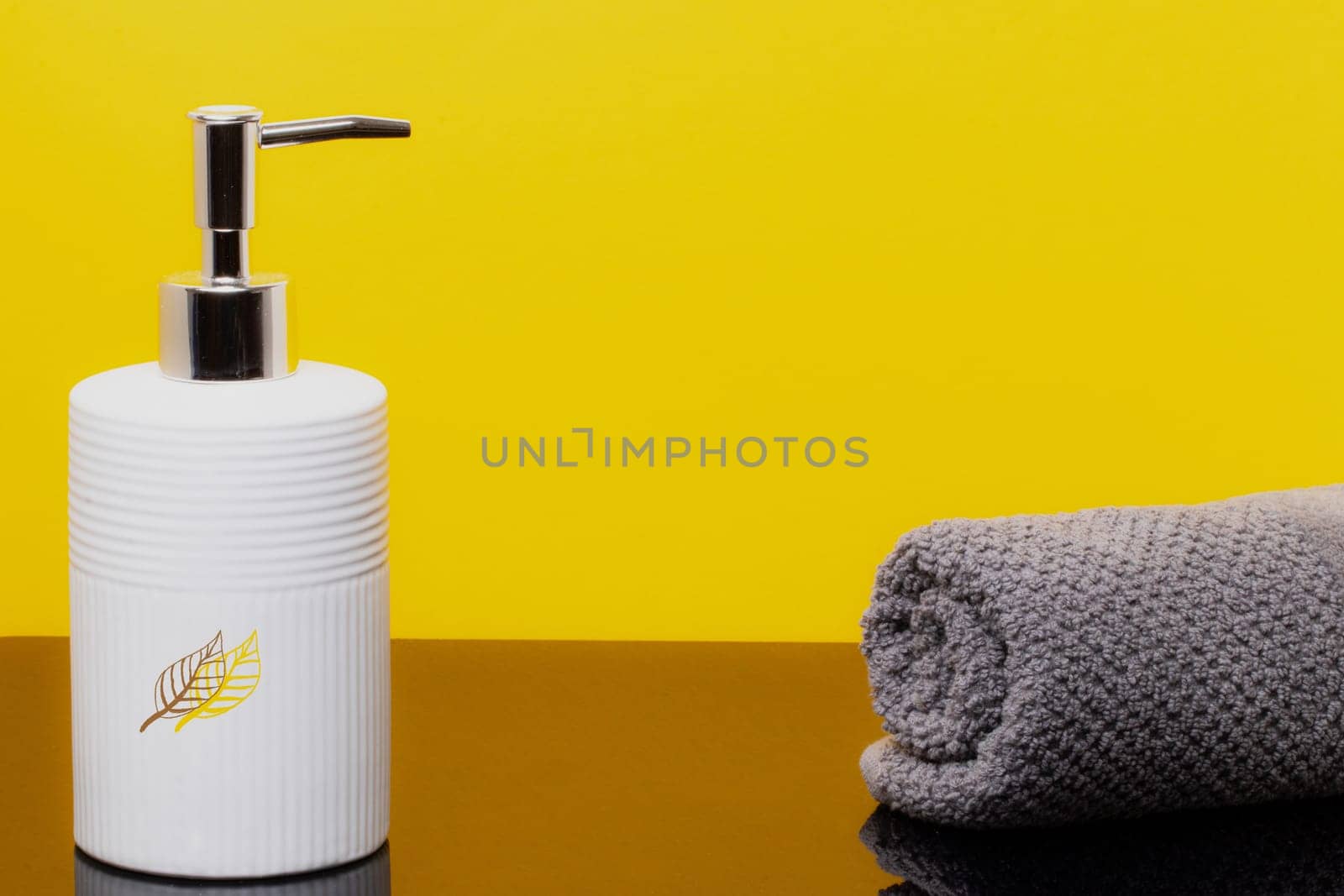Macro of a beauty cosmetic makeup bottle and a fresh soft terry bath towel on brown table over yellow background. Copy space for product display montage.