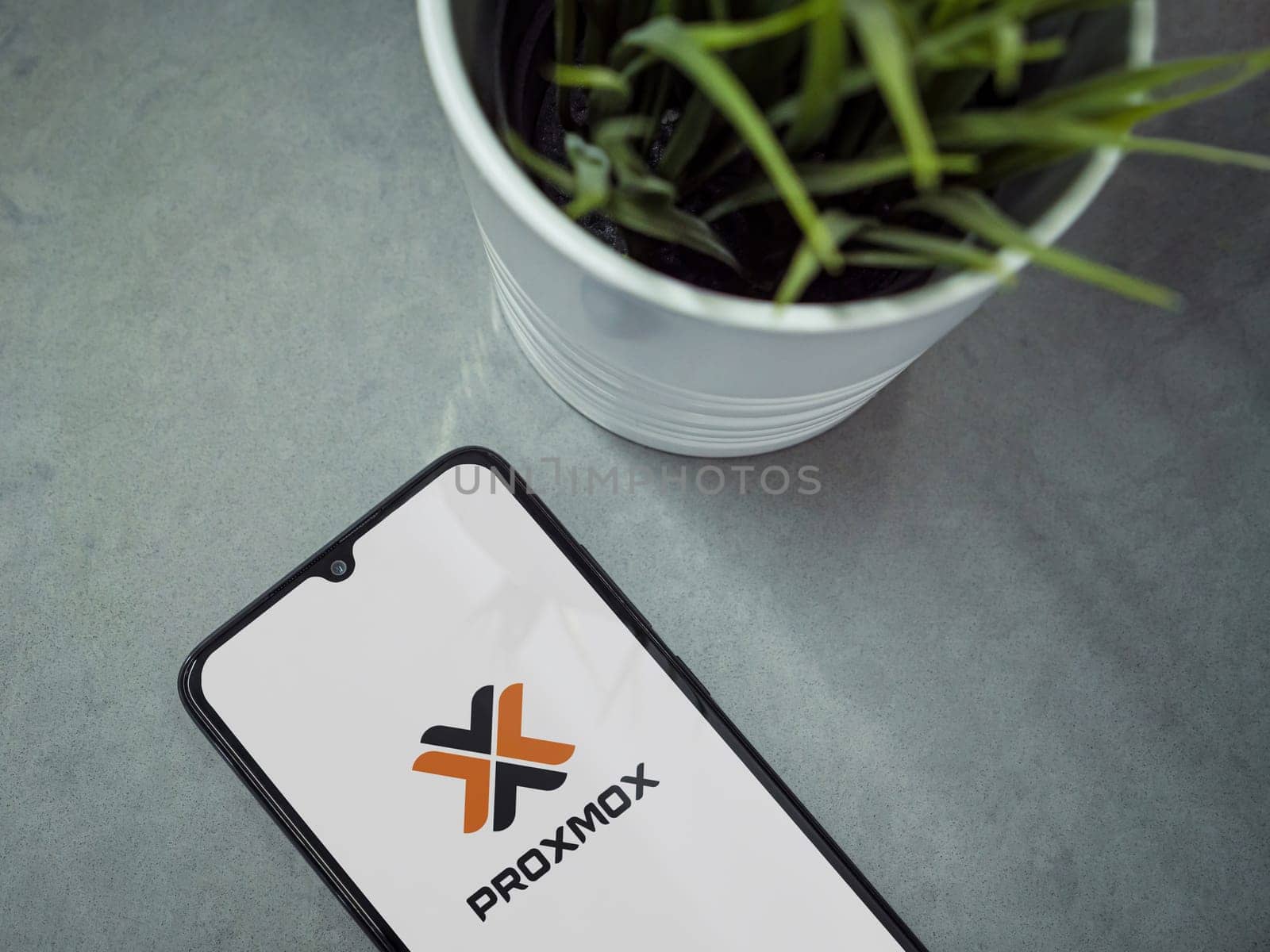 Lod, Israel - July 16,2023: Modern workspace with smartphone with Proxmox Virtual Environment app launch screen on marble background. Close up top view flat lay.