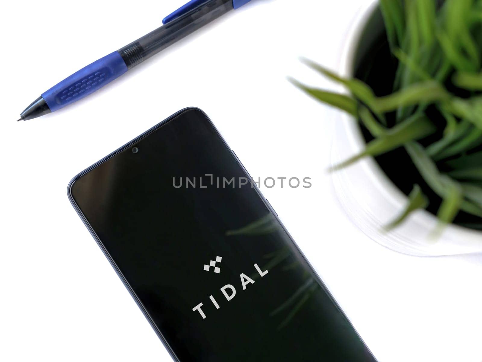Lod, Israel - July 16,2023: Modern workspace with smartphone with TIDAL Music app launch screen on white background. Close up top view flat lay.