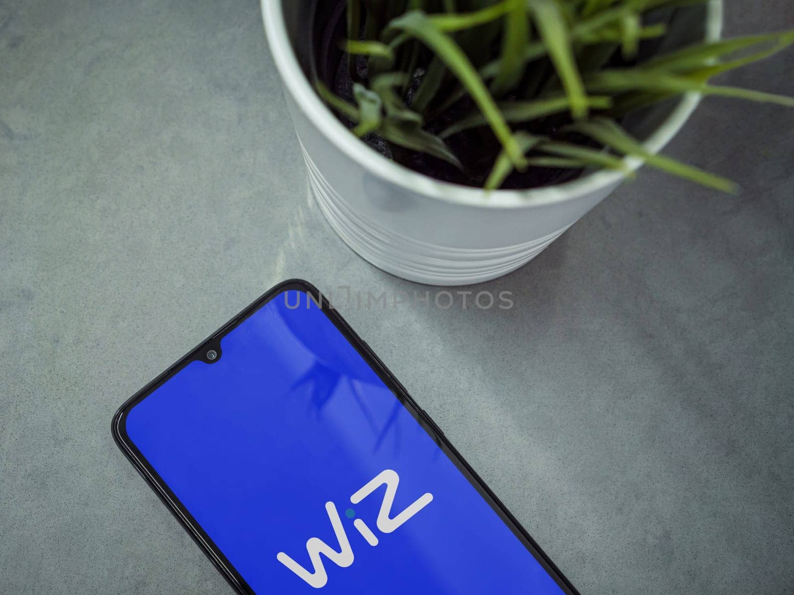 Lod, Israel - July 16,2023: Modern workspace with smartphone with WIZ app launch screen on marble background. Close up top view flat lay.