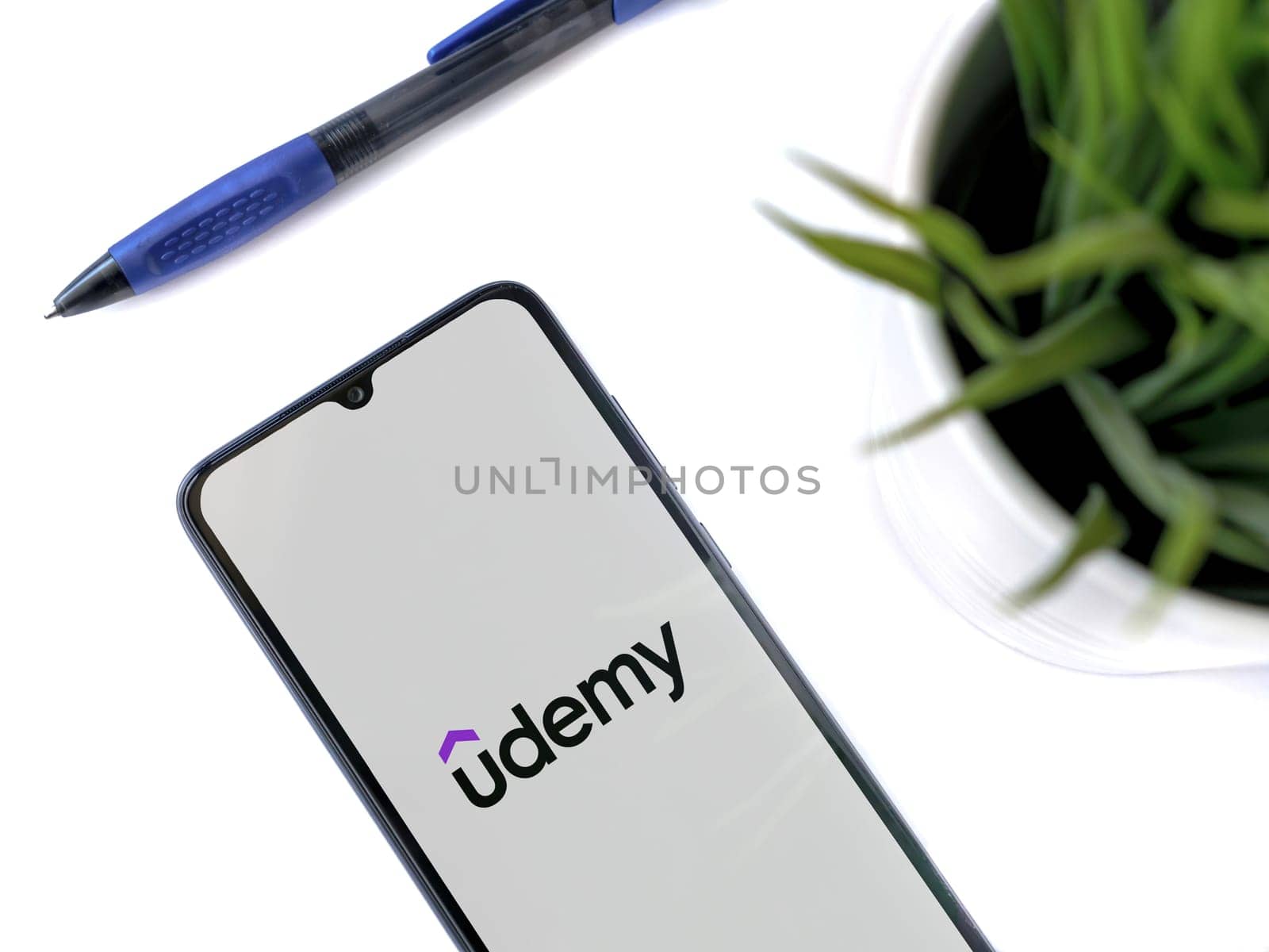 Lod, Israel - July 16,2023: Modern workspace with smartphone with Udemy app launch screen on white background. Close up top view flat lay.