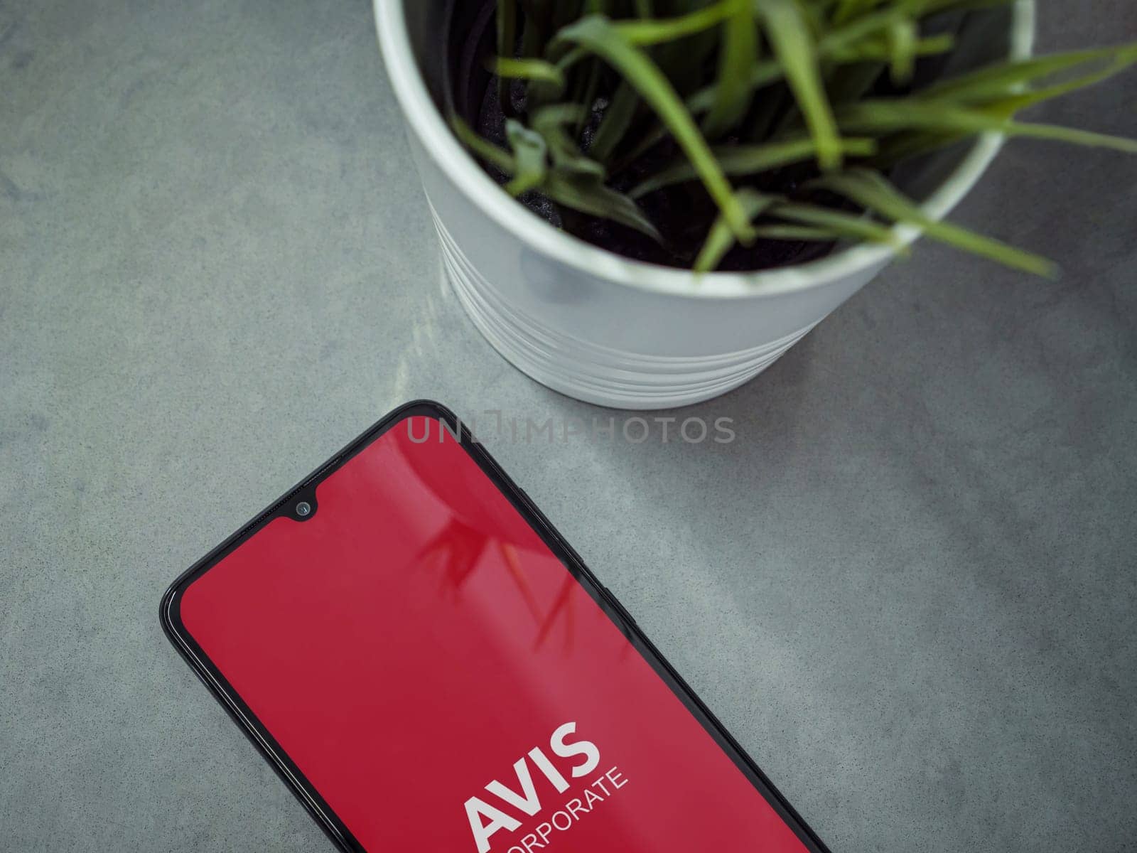 Lod, Israel - July 16,2023: Modern workspace with smartphone with Avis Corporate app launch screen on marble background. Close up top view flat lay.
