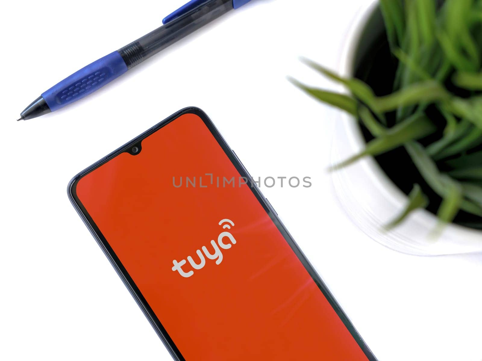 Lod, Israel - July 16,2023: Modern workspace with smartphone with Tuya Smart app launch screen on white background. Close up top view flat lay.