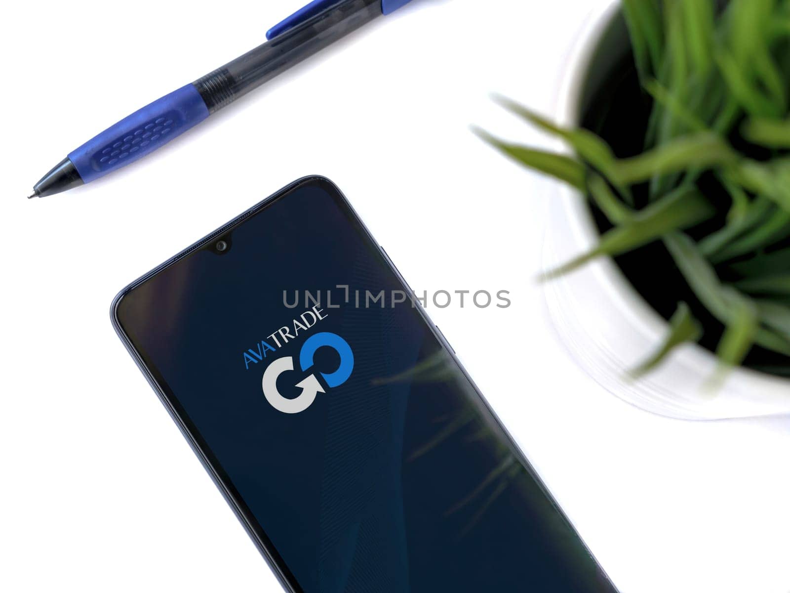Lod, Israel - July 16,2023: Modern workspace with smartphone with Avatrade app launch screen on white background. Close up top view flat lay.