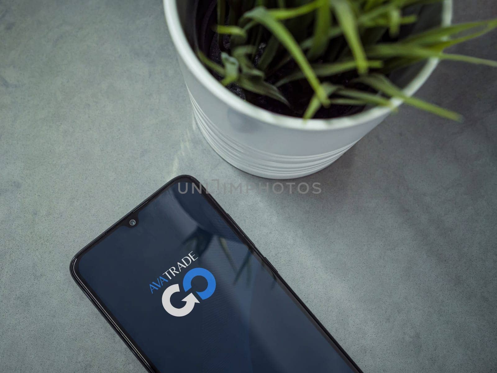 Lod, Israel - July 16,2023: Modern workspace with smartphone with Avatrade app launch screen on marble background. Close up top view flat lay.