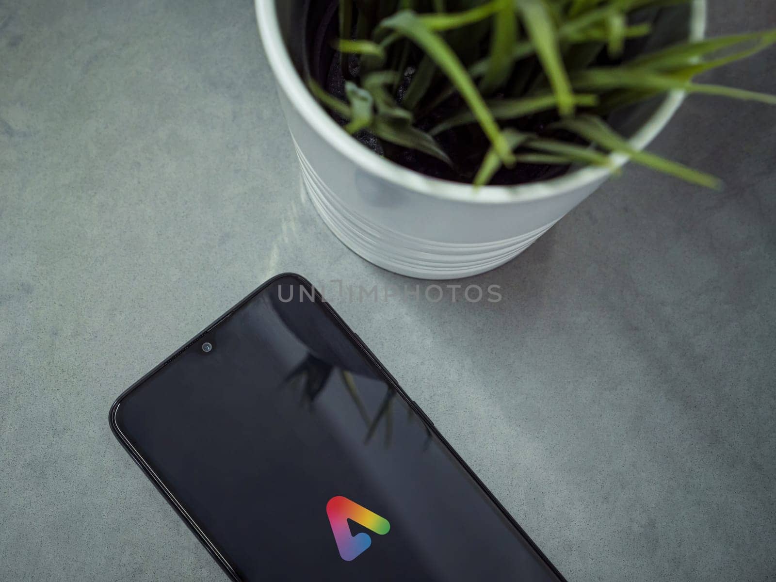 Lod, Israel - July 16,2023: Modern workspace with smartphone with Adobe Express - Graphic Design app launch screen on marble background. Close up top view flat lay.