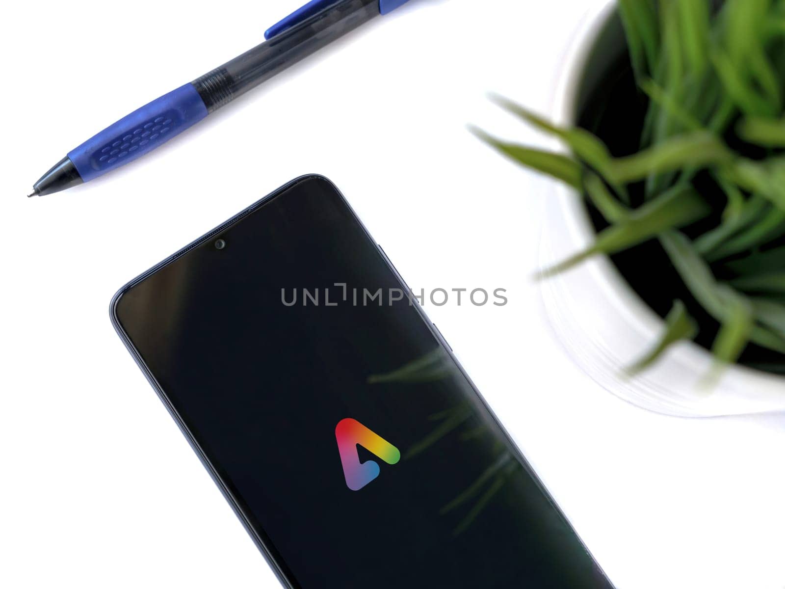 Lod, Israel - July 16,2023: Modern workspace with smartphone with Adobe Express - Graphic Design app launch screen on white background. Close up top view flat lay.