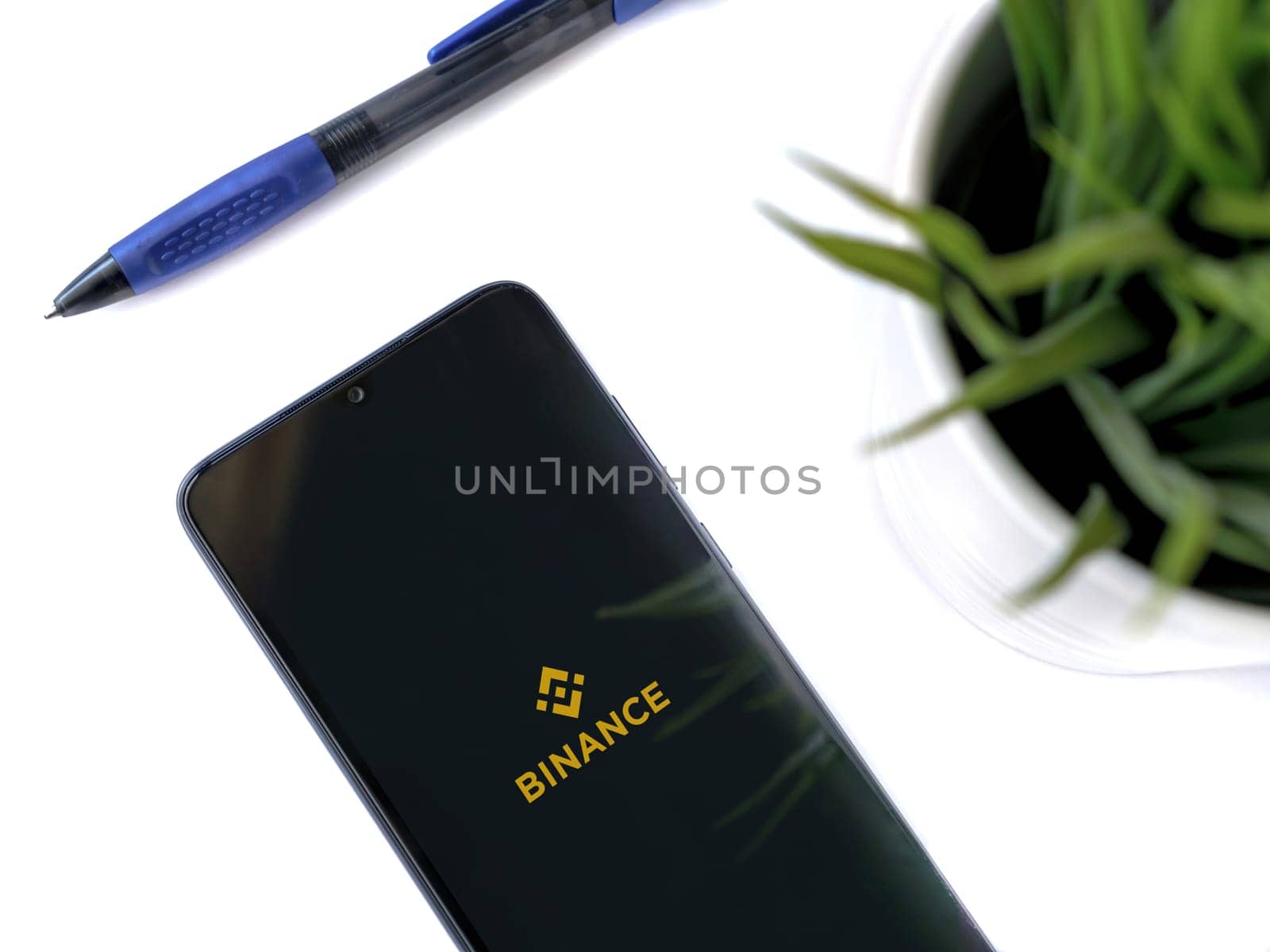 Lod, Israel - July 16,2023: Modern workspace with smartphone with Binance app launch screen on white background. Close up top view flat lay.