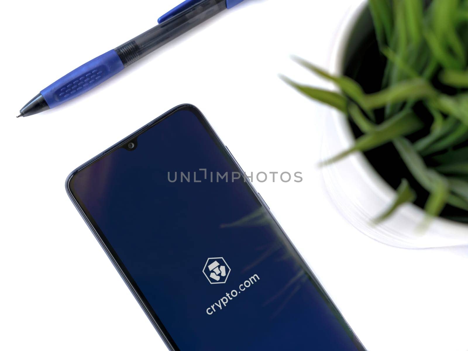 Lod, Israel - July 16,2023: Modern workspace with smartphone with Crypto.com app launch screen on white background. Close up top view flat lay.