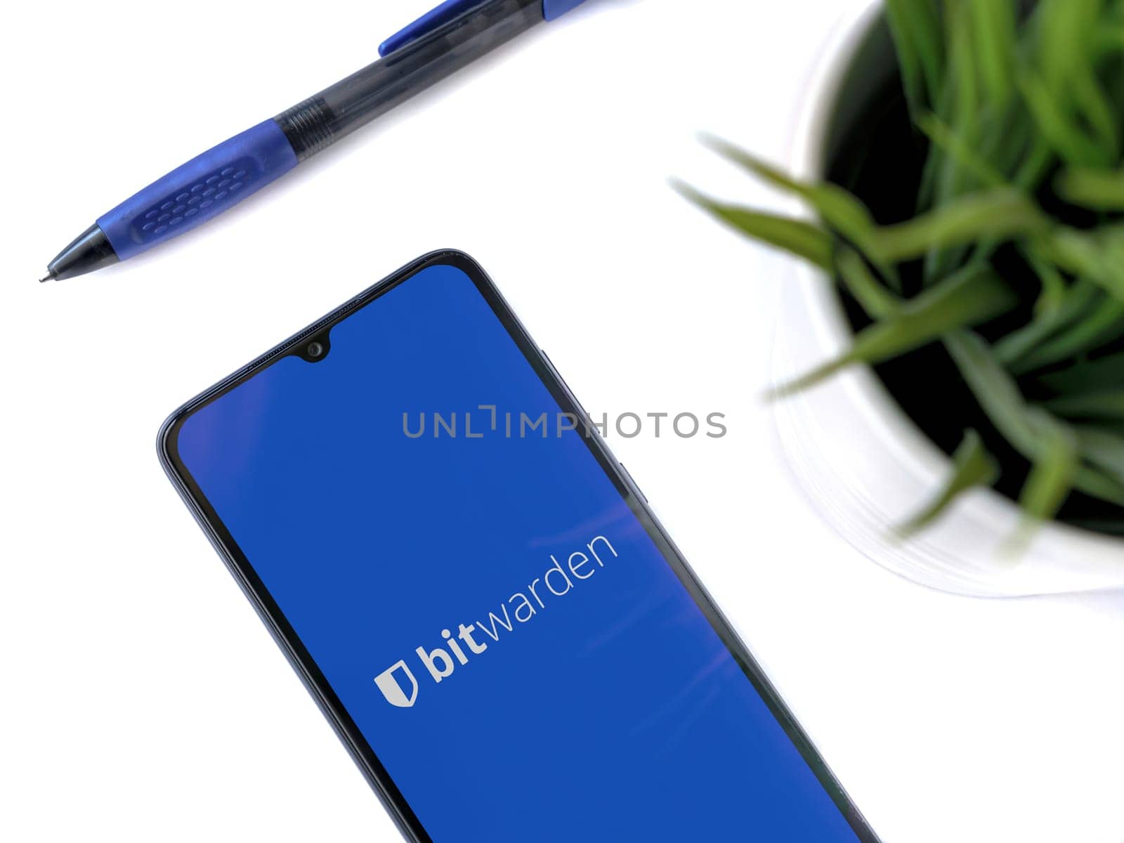 Lod, Israel - July 16,2023: Modern workspace with smartphone with Bitwarden Password Manager app launch screen on white background. Close up top view flat lay.