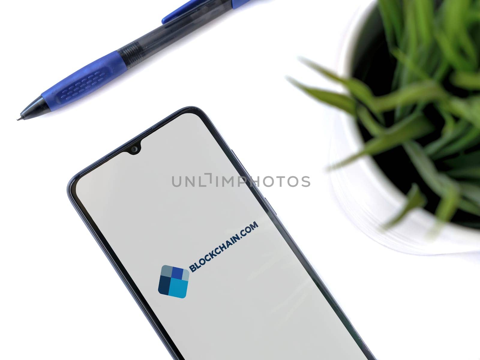 Lod, Israel - July 16,2023: Modern workspace with smartphone with Blockchain.com app launch screen on white background. Close up top view flat lay.