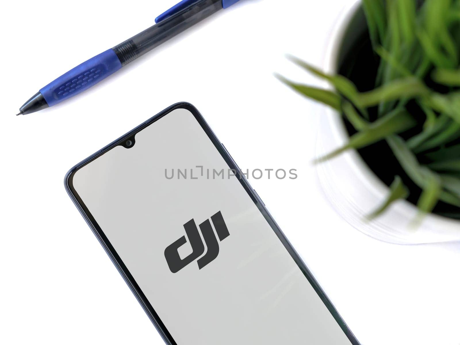 Lod, Israel - July 16,2023: Modern workspace with smartphone with DJI Store app launch screen on white background. Close up top view flat lay.