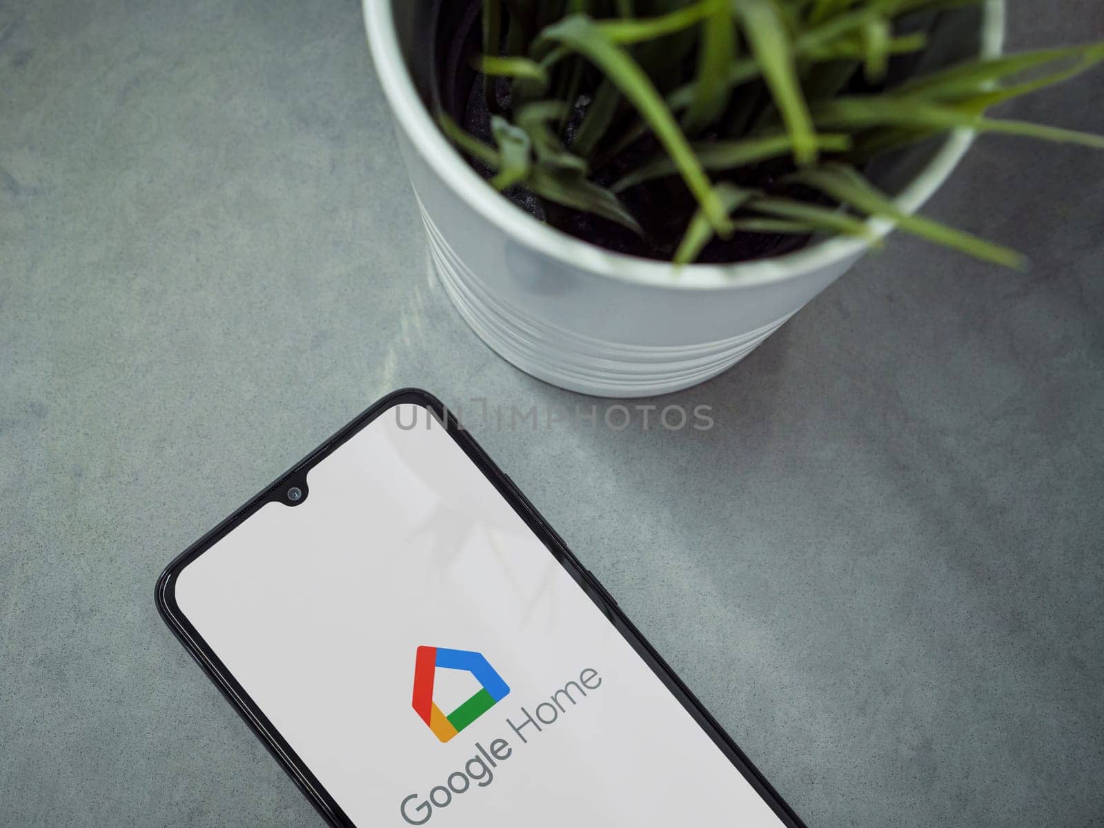 Lod, Israel - July 16,2023: Modern workspace with smartphone with Google Home app launch screen on marble background. Close up top view flat lay.