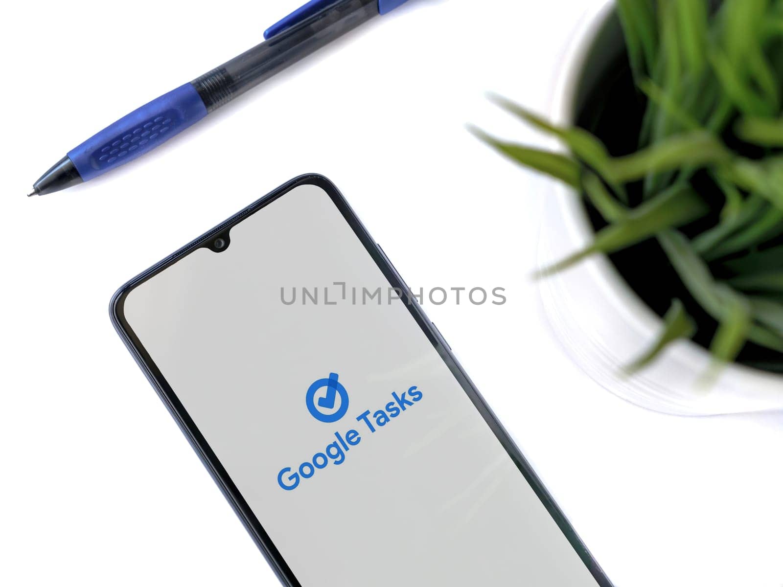 Lod, Israel - July 16,2023: Modern workspace with smartphone with Google Task app launch screen on white background. Close up top view flat lay.