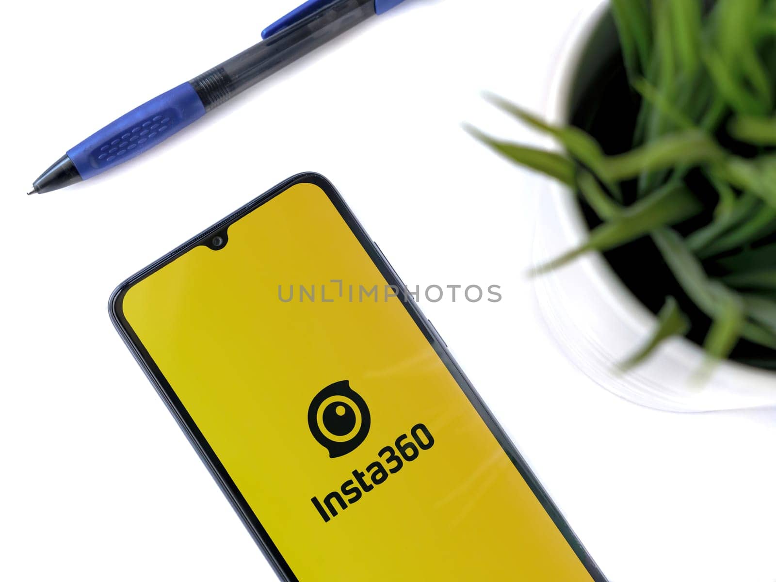 Lod, Israel - July 16,2023: Modern workspace with smartphone with Insta360 app launch screen on white background. Close up top view flat lay.
