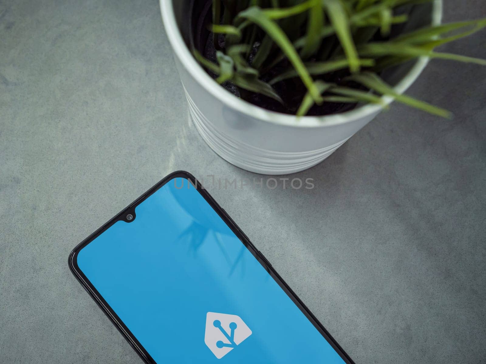 Lod, Israel - July 16,2023: Modern workspace with smartphone with Home Assistant app launch screen on marble background. Close up top view flat lay.