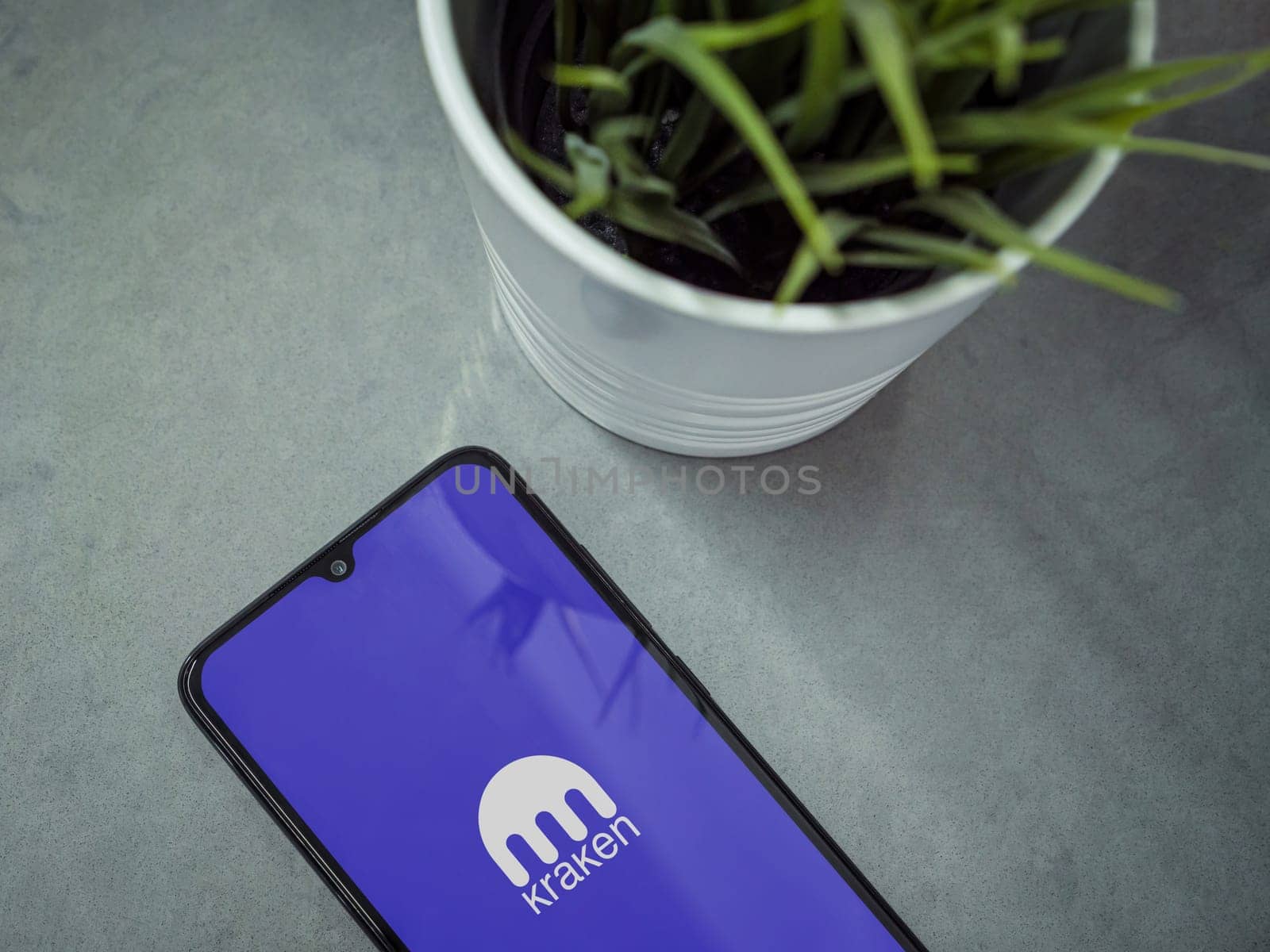 Lod, Israel - July 16,2023: Modern workspace with smartphone with Kraken app launch screen on marble background. Close up top view flat lay.