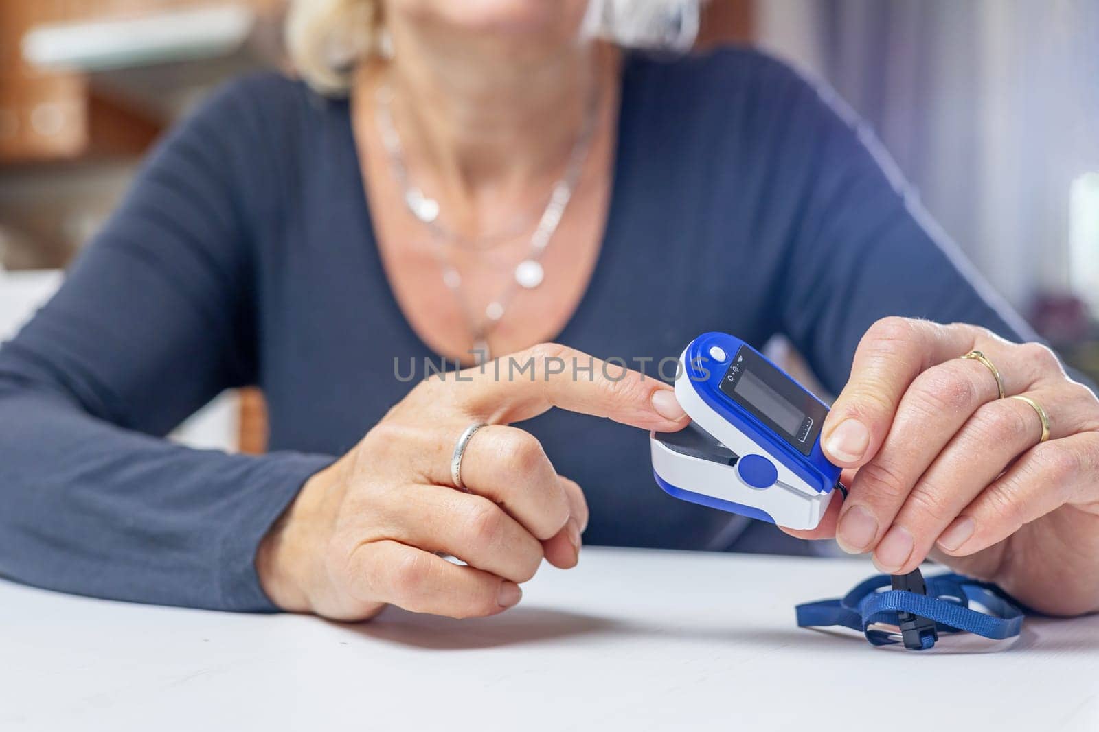 Woman is inserting finger into compact electronic pulse oximeter.  Horizontally.