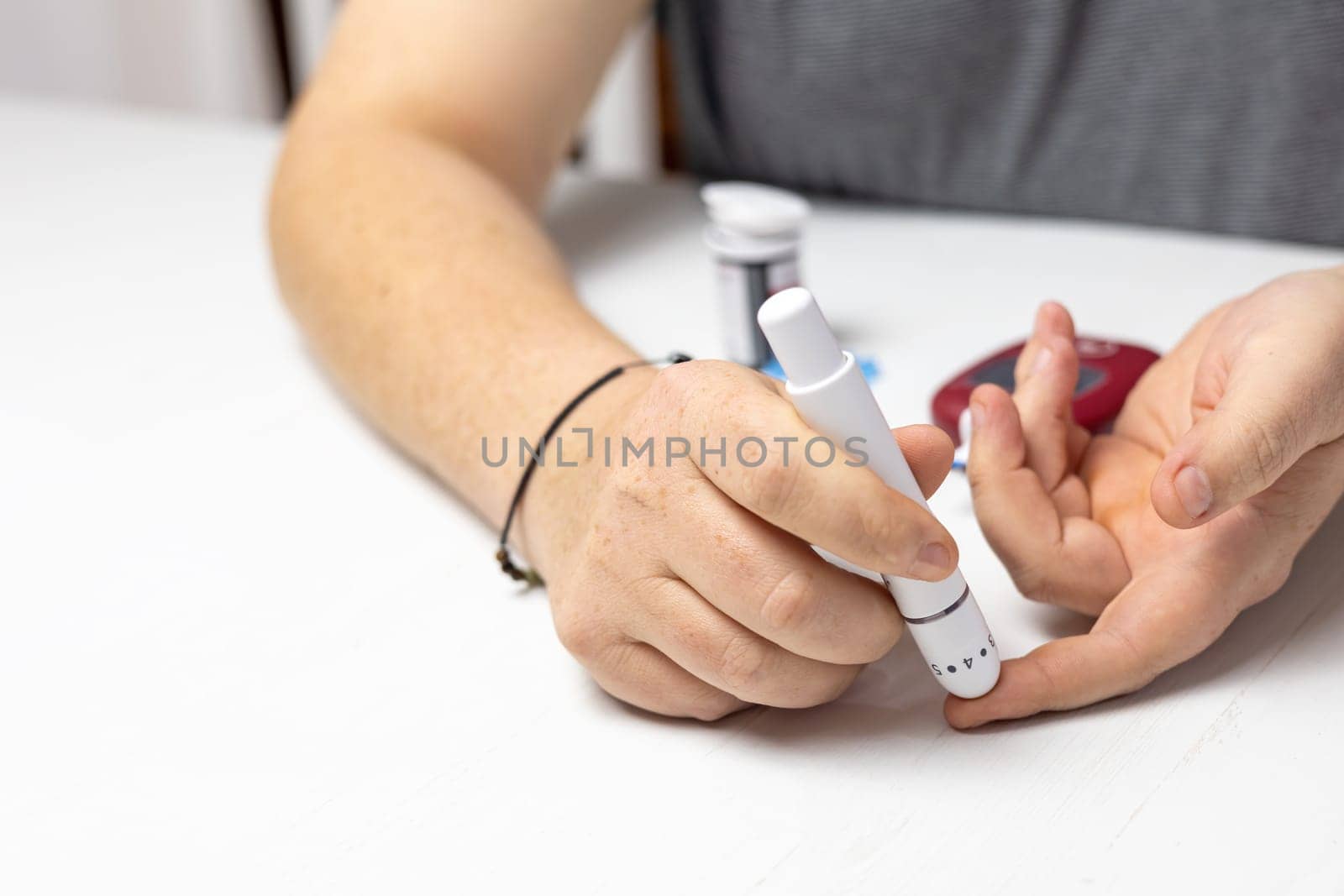 Male hands use an adjustable lancing device. Horizontally.