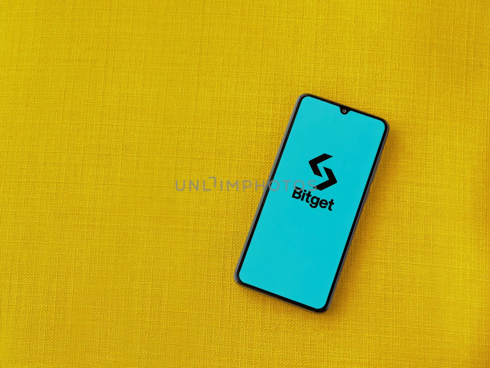 Lod, Israel - July 16,2023: Bitget app launch screen on smartphone on yellow fabric background. Top view flat lay with copy space.