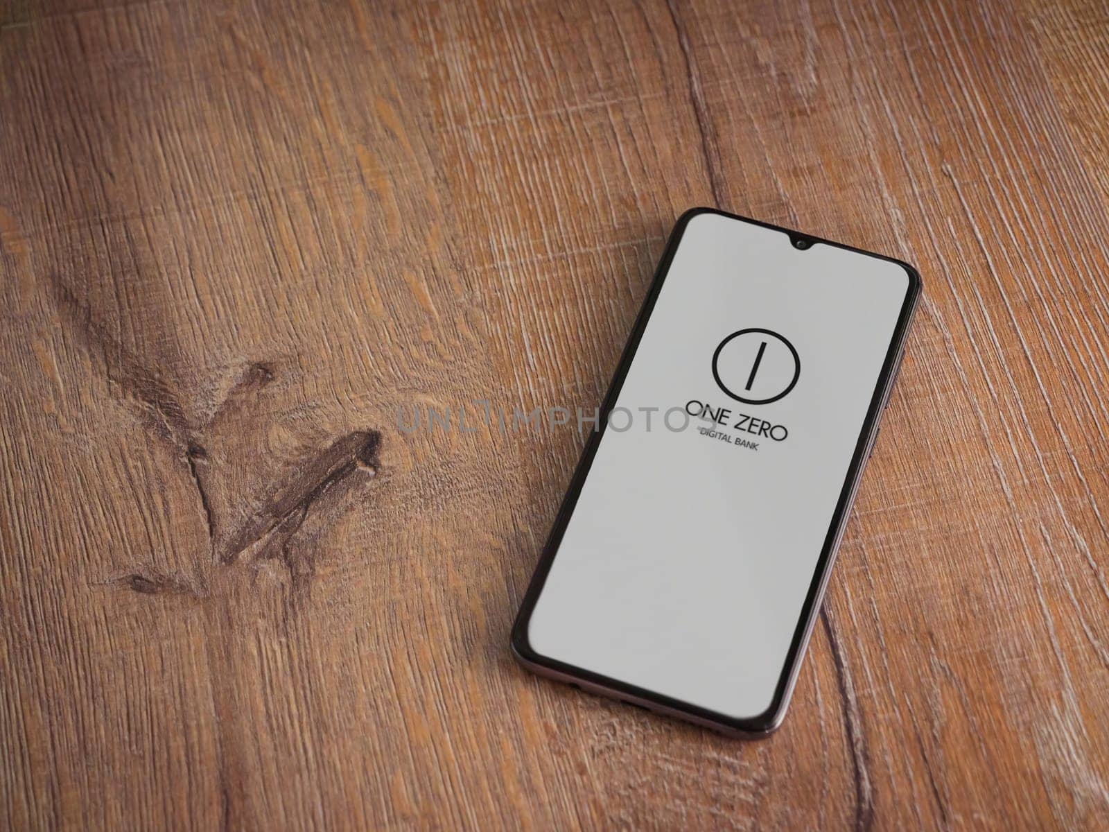 Lod, Israel - July 16,2023: One Zero app launch screen on smartphone on wooden background. Top view flat lay with copy space.