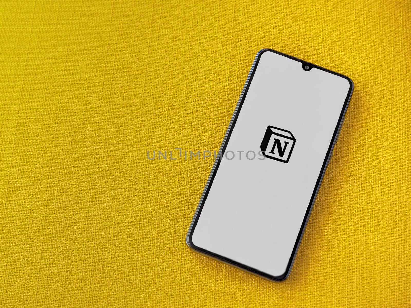 Lod, Israel - July 16,2023: Notion app launch screen on smartphone on yellow fabric background. Top view flat lay with copy space.
