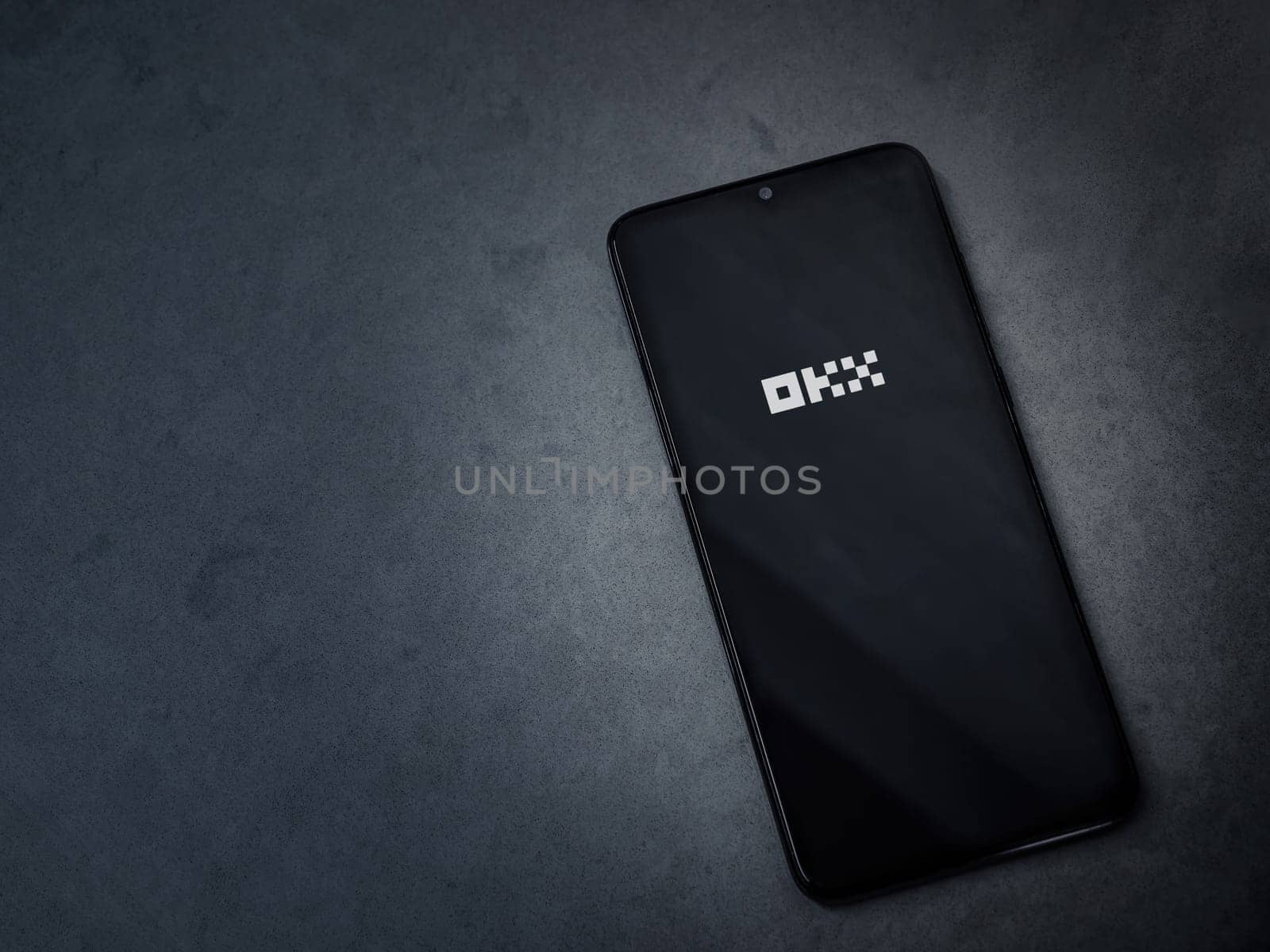 Lod, Israel - July 16,2023: OKX app launch screen on smartphone on dark marble stone background. Top view flat lay with copy space.
