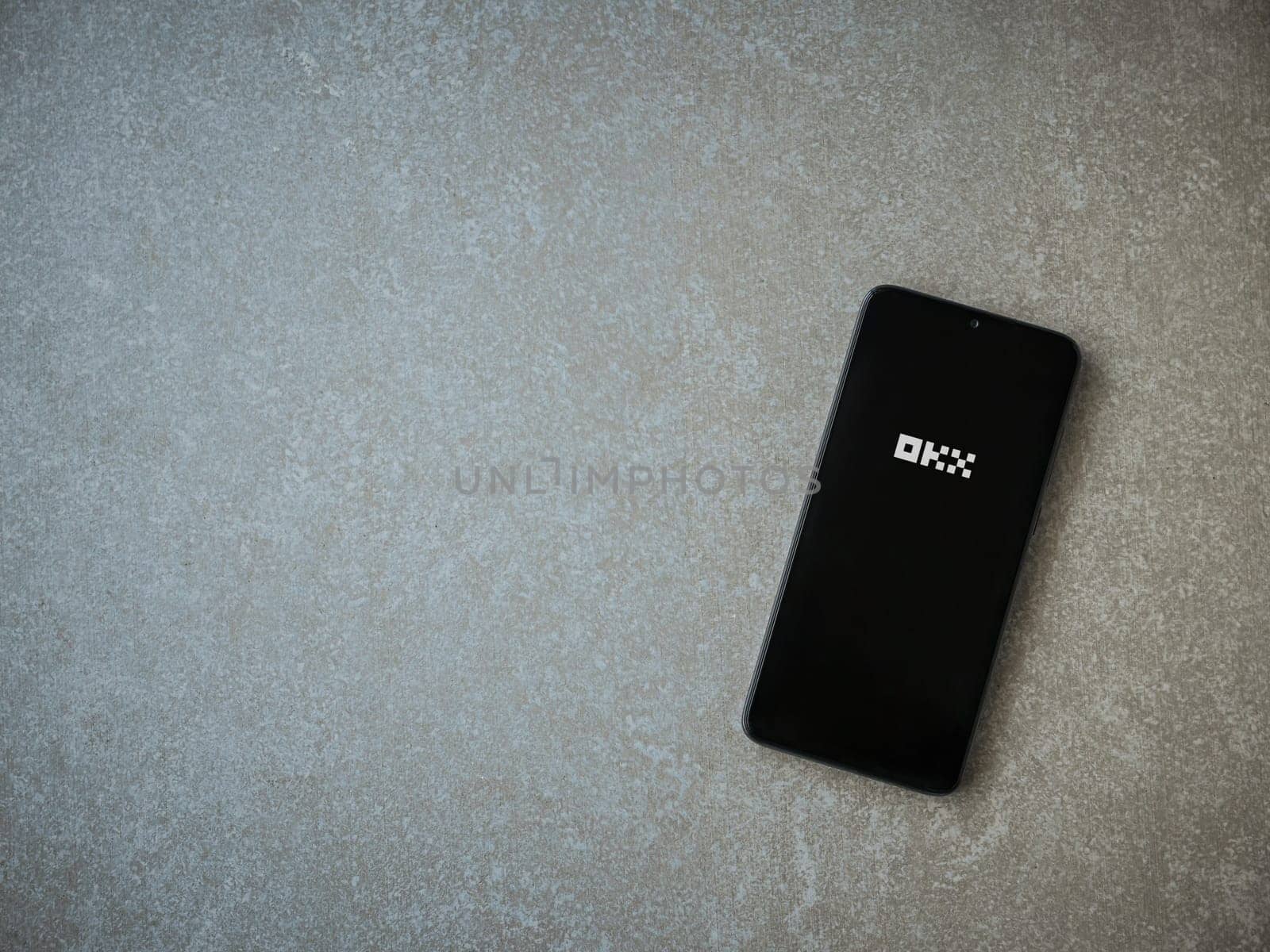 Lod, Israel - July 16,2023: OKX app launch screen on smartphone on ceramic stone background. Top view flat lay with copy space.