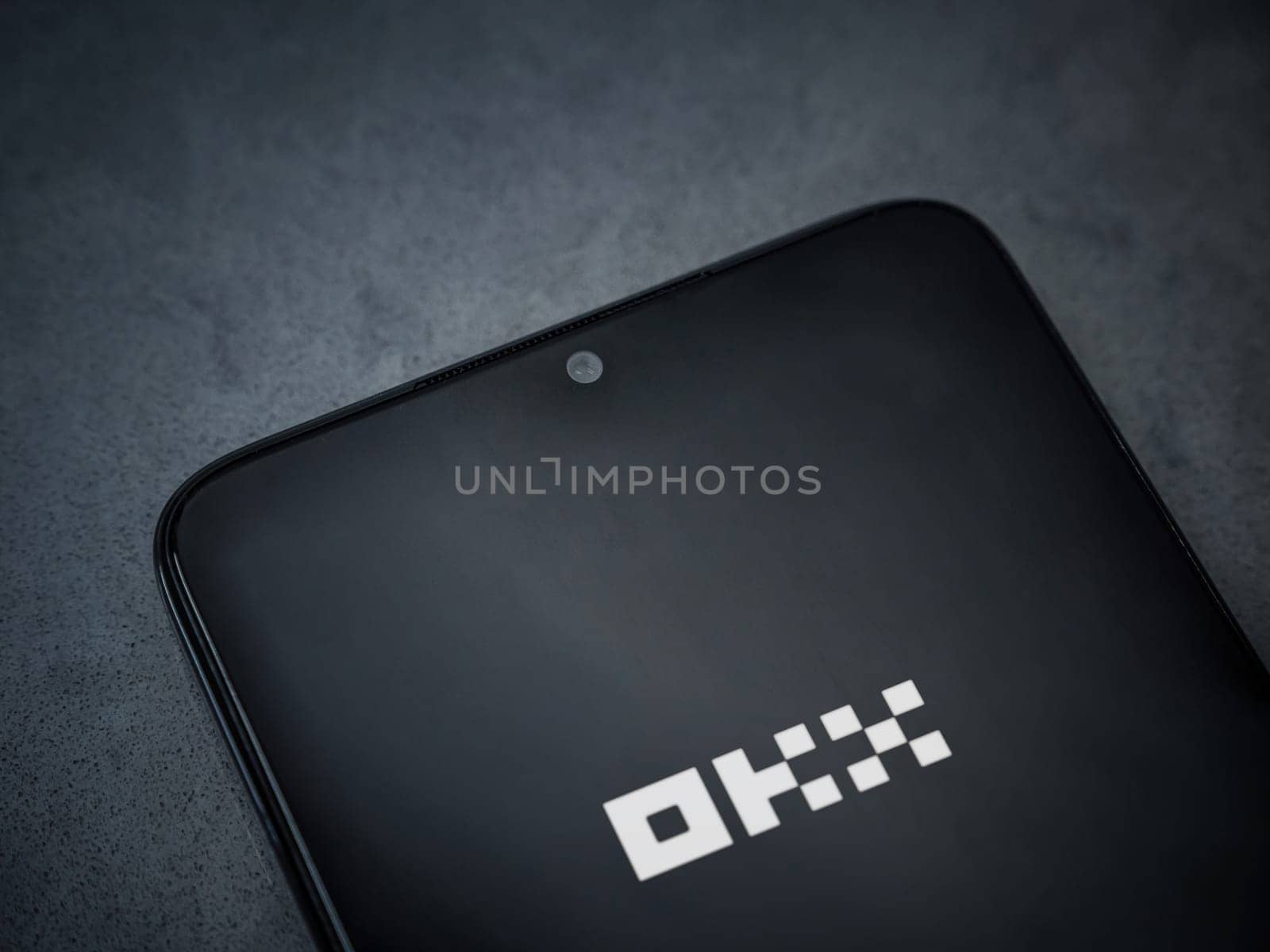 Lod, Israel - July 16,2023: OKX app launch screen on smartphone on dark marble stone background. Top view flat lay with copy space.