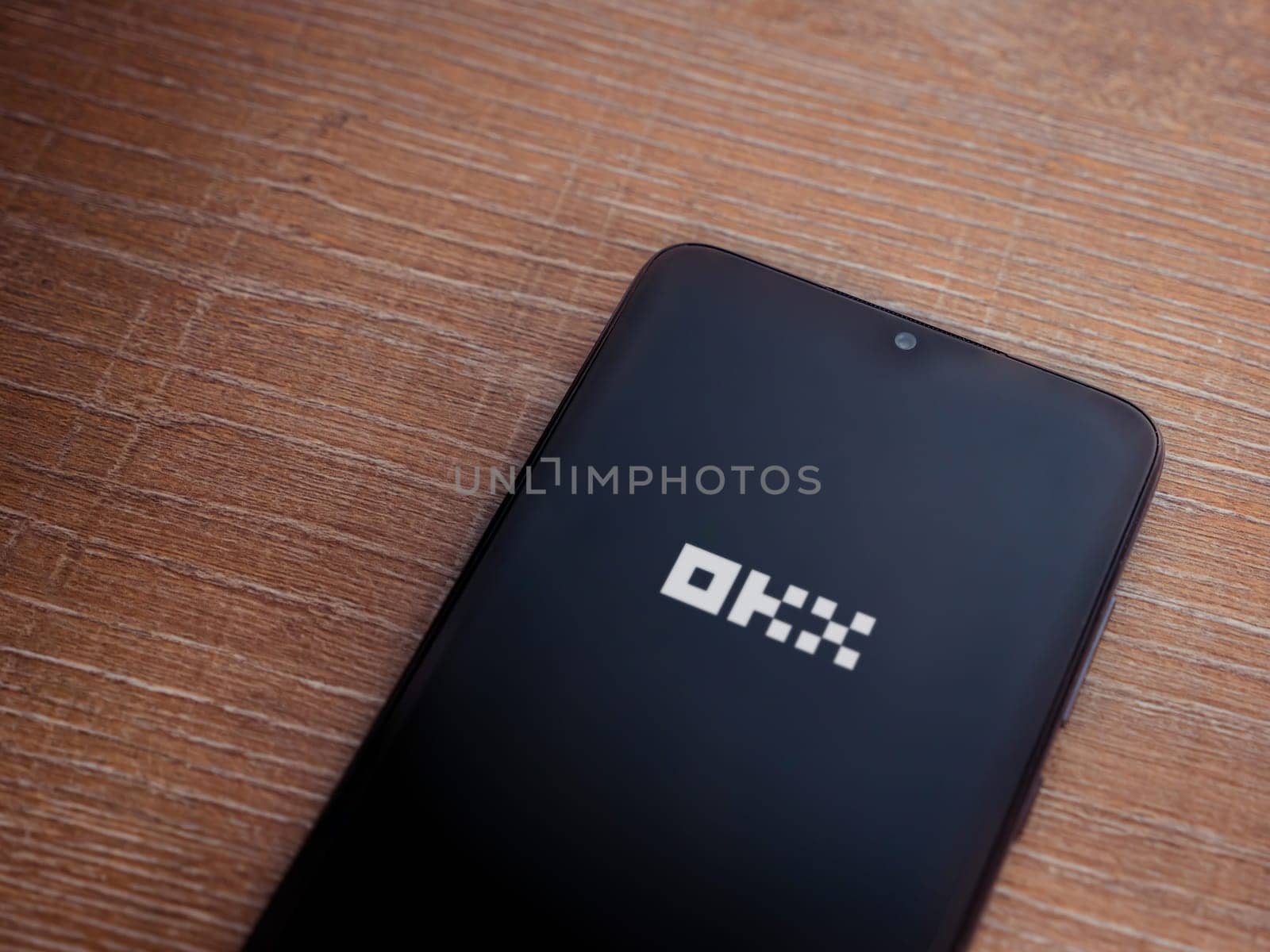 Lod, Israel - July 16,2023: OKX app launch screen on smartphone on wooden background. Top view flat lay with copy space.