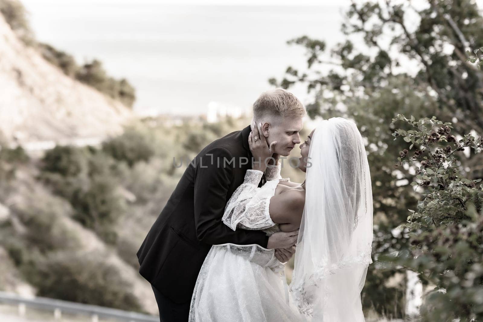 Happy newlyweds kiss against the backdrop of a beautiful mountain landscape, sepia