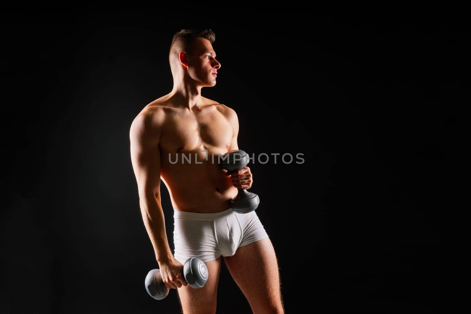 Shirtless bodybuilder holding a dumbell and showing his muscular arms.