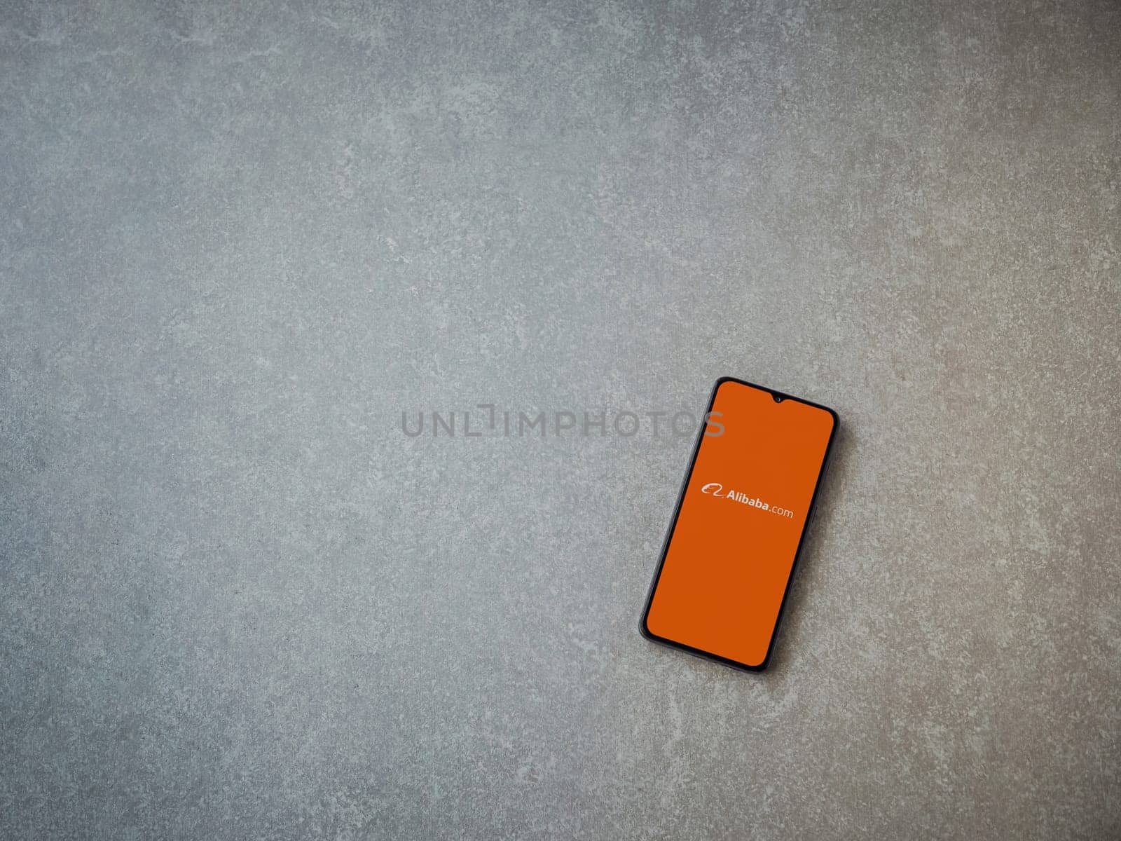 Lod, Israel - July 16,2023: Alibaba.com app launch screen on smartphone on ceramic stone background. Top view flat lay with copy space.
