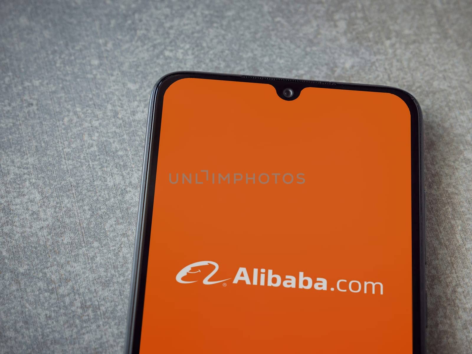 Lod, Israel - July 16,2023: Alibaba.com app launch screen on smartphone on ceramic stone background. Top view flat lay with copy space.