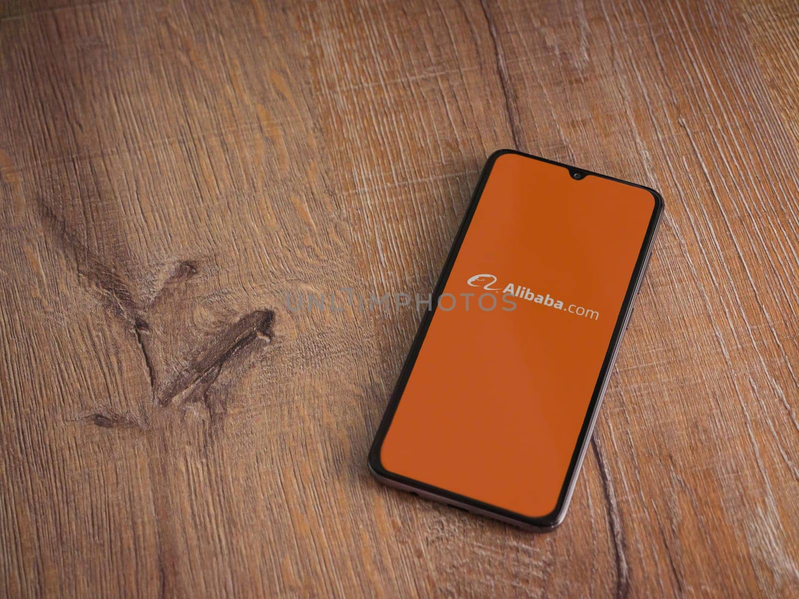 Lod, Israel - July 16,2023: Alibaba.com app launch screen on smartphone on wooden background. Top view flat lay with copy space.