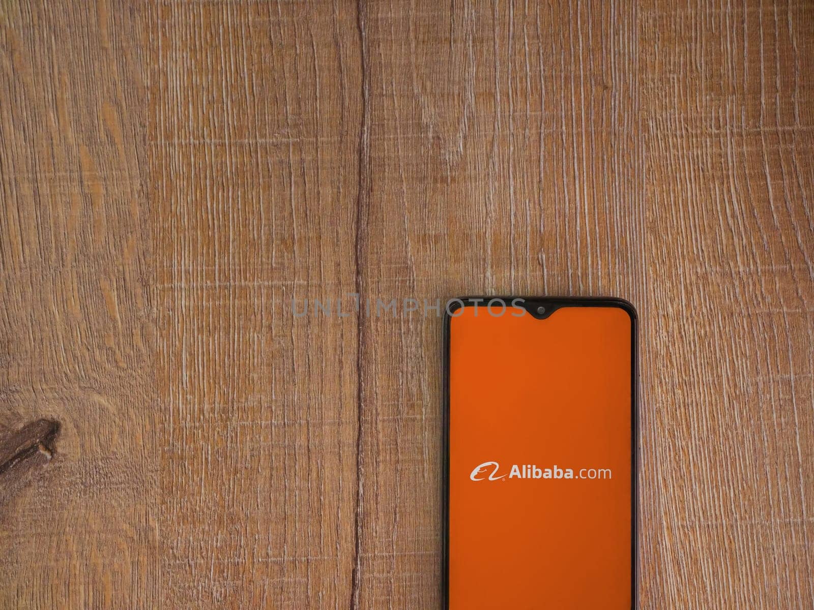 Lod, Israel - July 16,2023: Alibaba.com app launch screen on smartphone on wooden background. Top view flat lay with copy space.