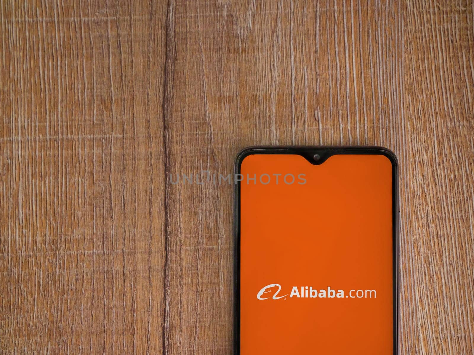Lod, Israel - July 16,2023: Alibaba.com app launch screen on smartphone on wooden background. Top view flat lay with copy space.