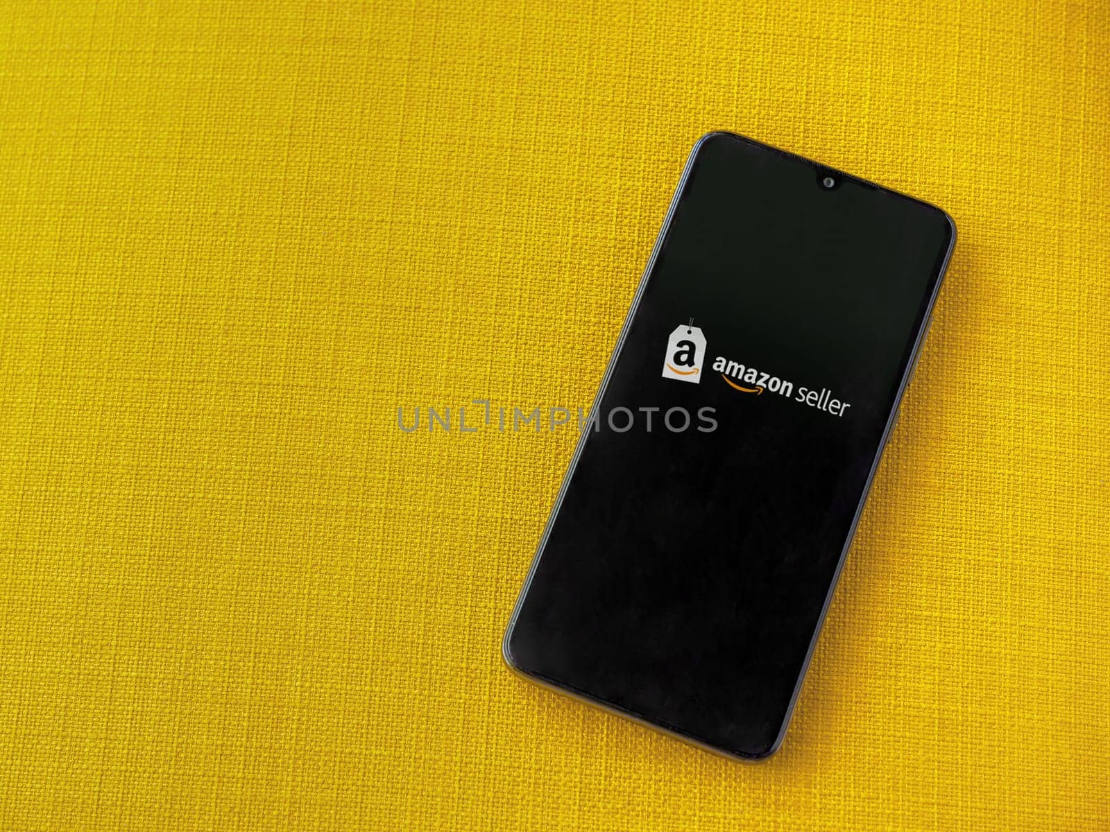 Lod, Israel - July 16,2023: Amazon Seller app launch screen on smartphone on yellow fabric background. Top view flat lay with copy space.