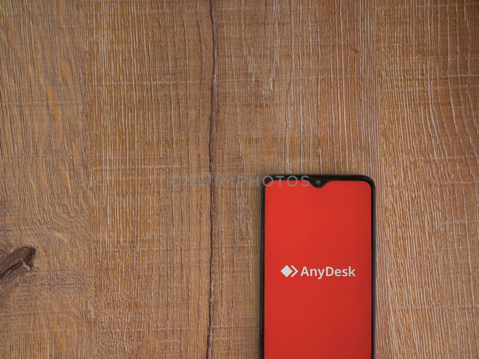 Lod, Israel - July 16,2023: Anydesk app launch screen on smartphone on wooden background. Top view flat lay with copy space.