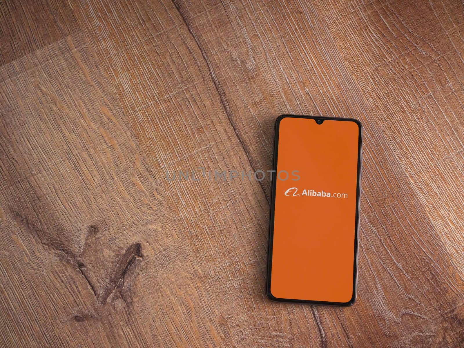 Lod, Israel - July 16,2023: Alibaba.com app launch screen on smartphone on wooden background. Top view flat lay with copy space.